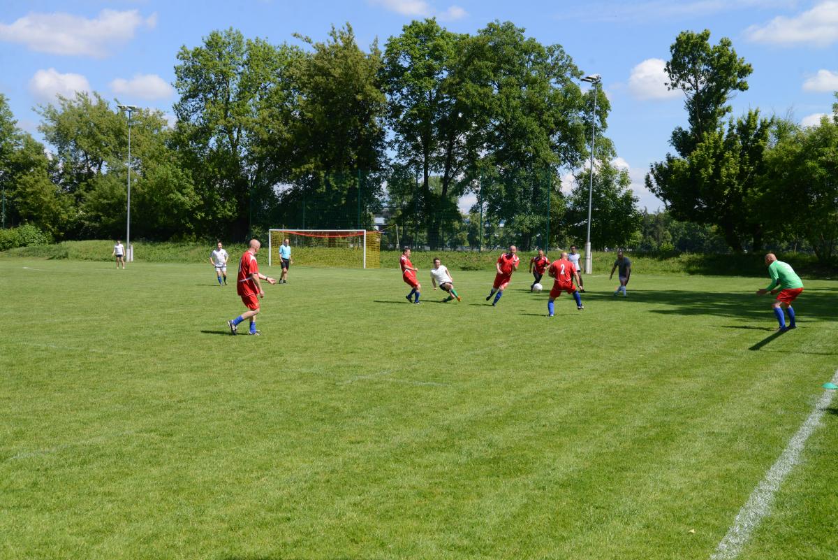 Zdjęcie nr: 13-DSC_3254 przedstawia odbywający się na murawie mecz piłkarski drużyn ubranych w jasnoczarne stroje oraz w stroje czerwone. Bramkarz przyjmuje postawę obrony przed golem.
