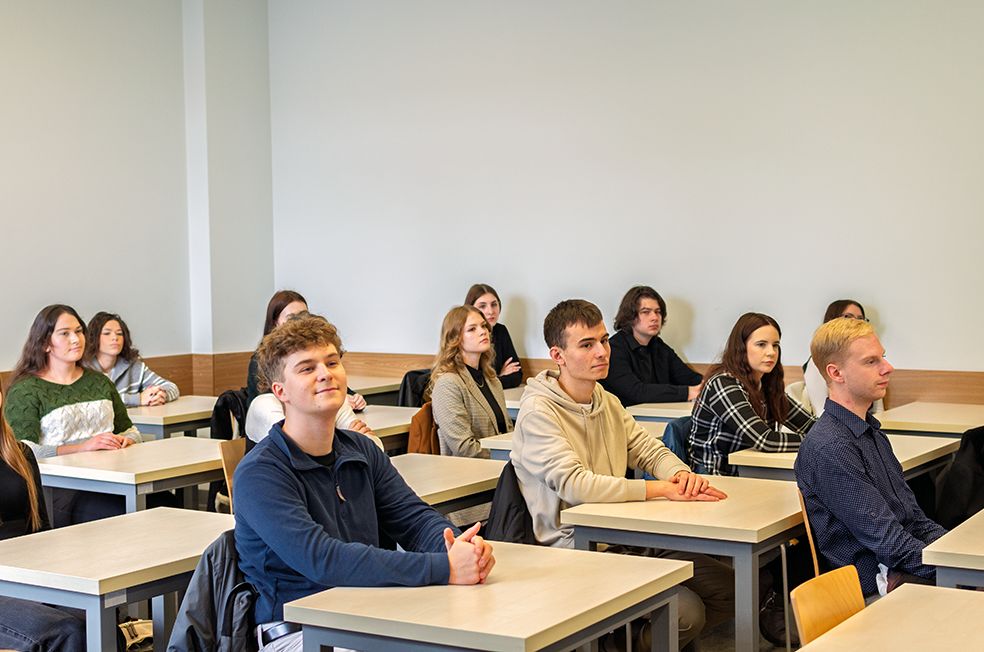 grupa dwunastu osób - czterech mężczyzn i ośmiu kobiet siedzących przy stolikach. 