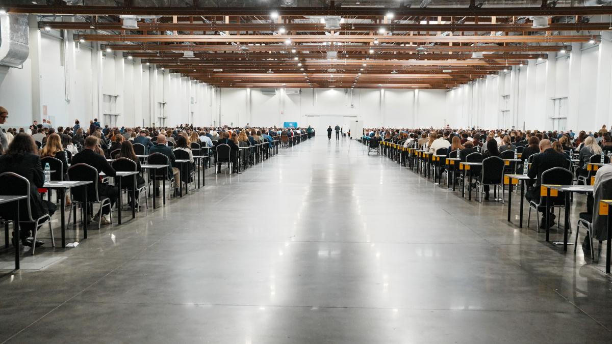 na zdjęciu widać salę, na krzesłach siedzą mężczyźni i kobiety, którzy są uczestnikami konkursu naboru na aplikację.